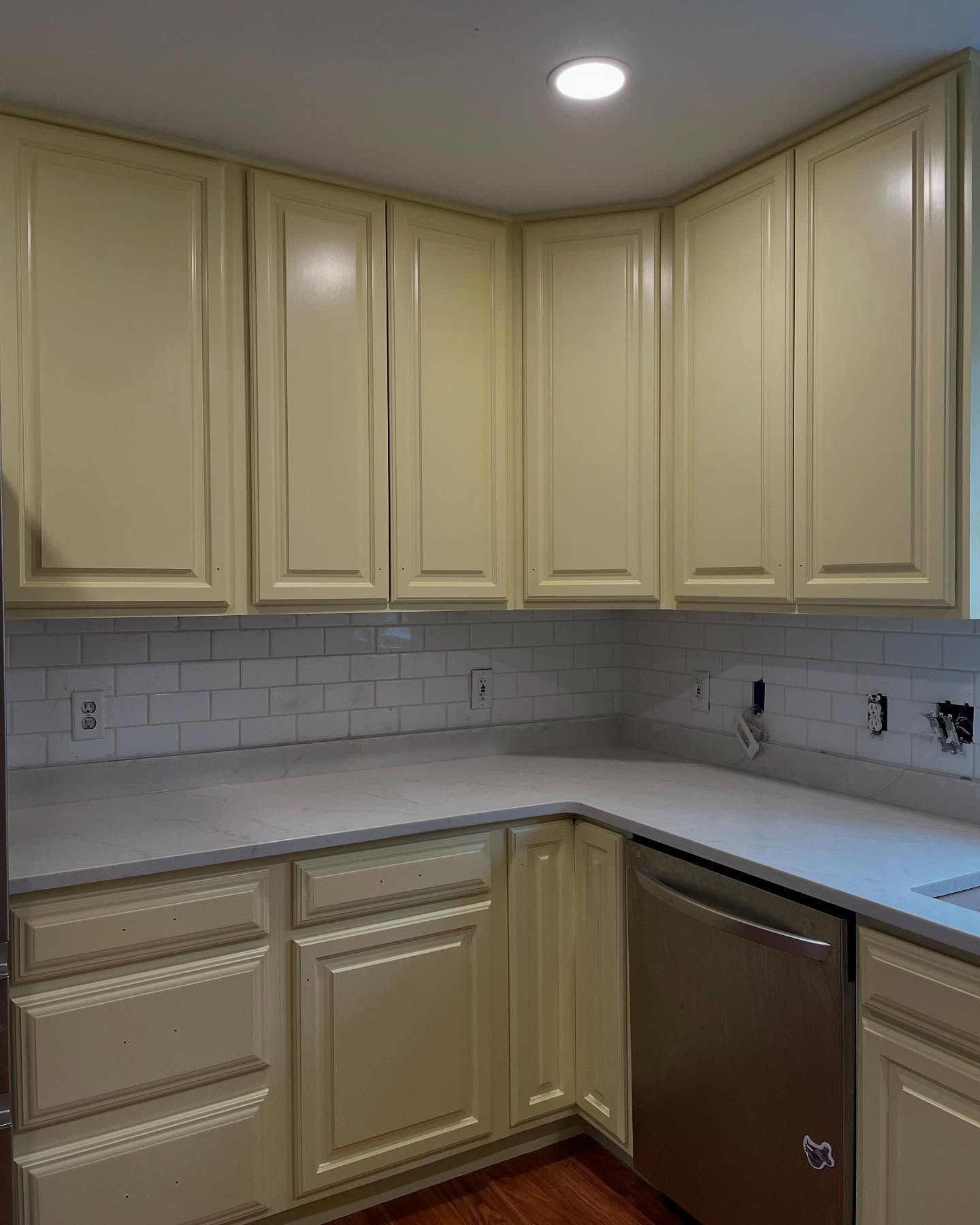 Kitchen with off-white cabinets, white tile backsplash, and light gray countertops. A stainless steel dishwasher is visible.