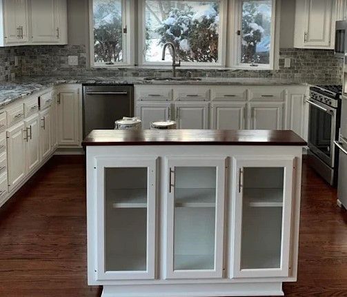 White kitchen with a dark wood island, light countertops, stainless steel appliances, and a window with a snowy view.