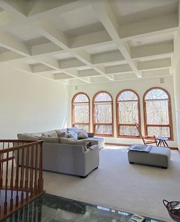 Spacious living room with high ceilings, a grid-like pattern, and arched windows. A beige sectional sofa, ottoman, and chair are visible.