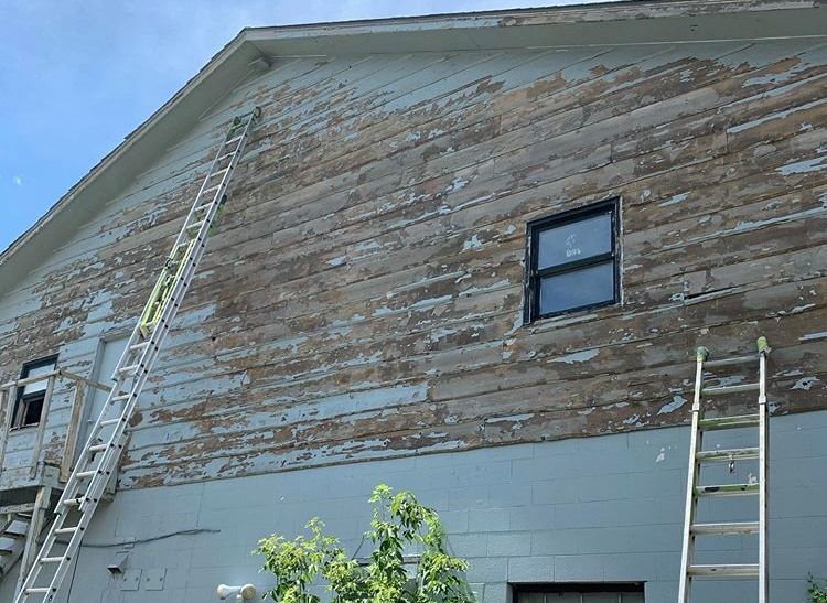 Building with peeling paint, multiple ladders leaning against it. The sky is blue.