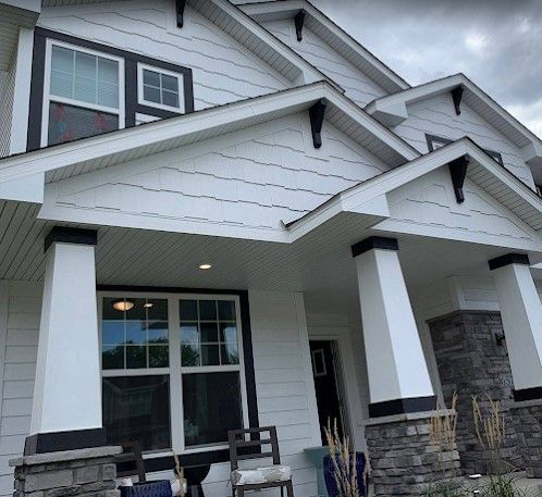 White house with black trim, stone accents, and multiple gabled roofs.  A porch has square pillars.