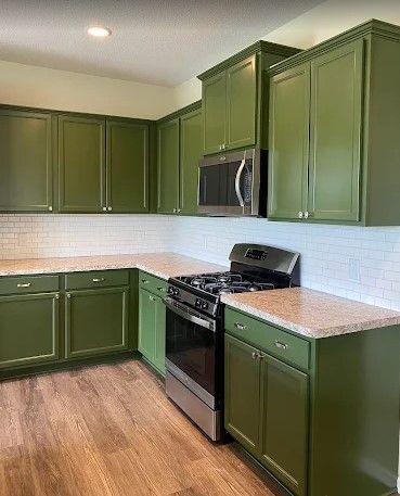 Green kitchen cabinets with light countertops and a stainless steel stove. White subway tile backsplash, and wood-look flooring.
