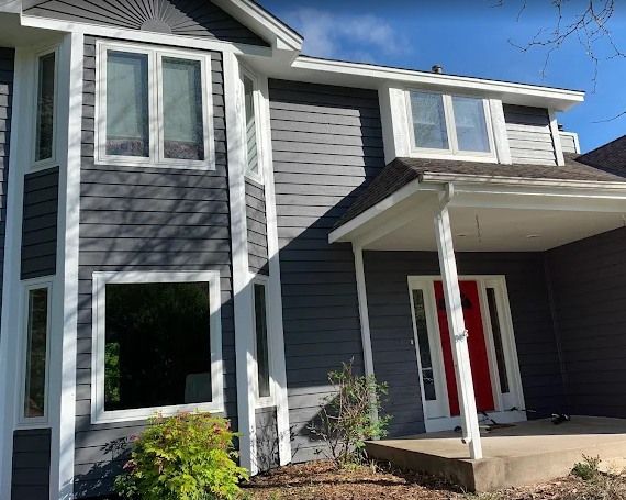 A two-story house with dark gray siding and white trim. A red door contrasts with the gray exterior.