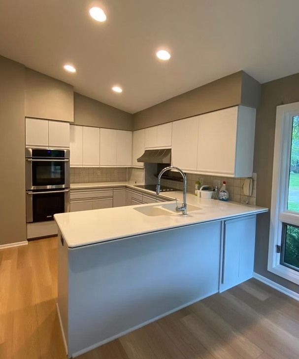 Modern kitchen with white cabinets, quartz countertops, and stainless steel appliances, featuring an island and hardwood floors.