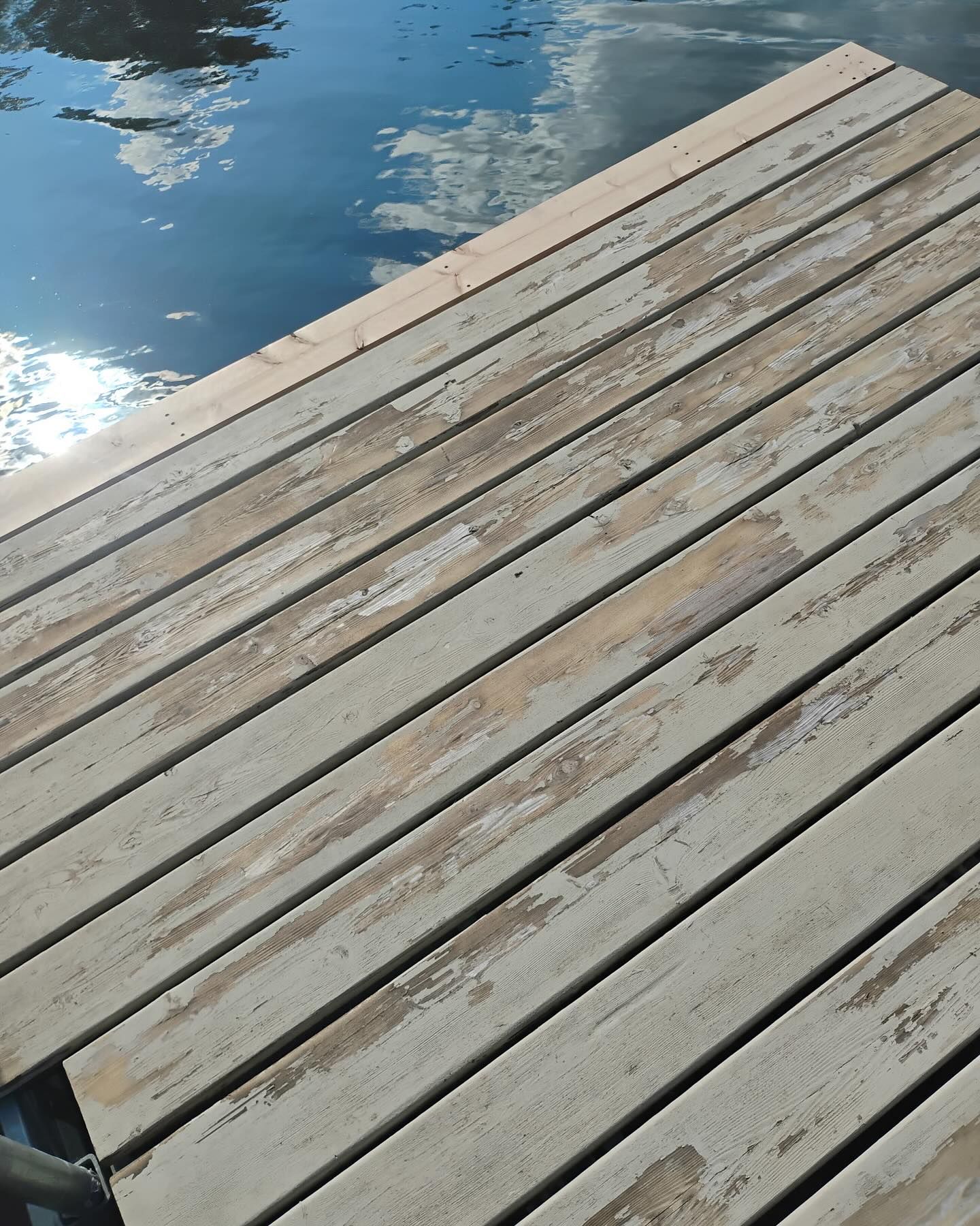 Weathered wooden dock planks angled toward water with reflections of sky.