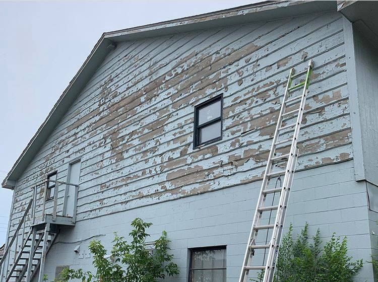 Exterior of a house with peeling blue paint, an extended ladder, and a metal fire escape.