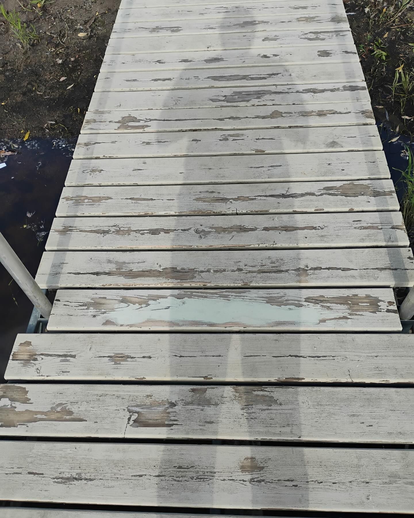 A weathered white wooden dock with peeling paint. A person's shadow is cast upon the surface.