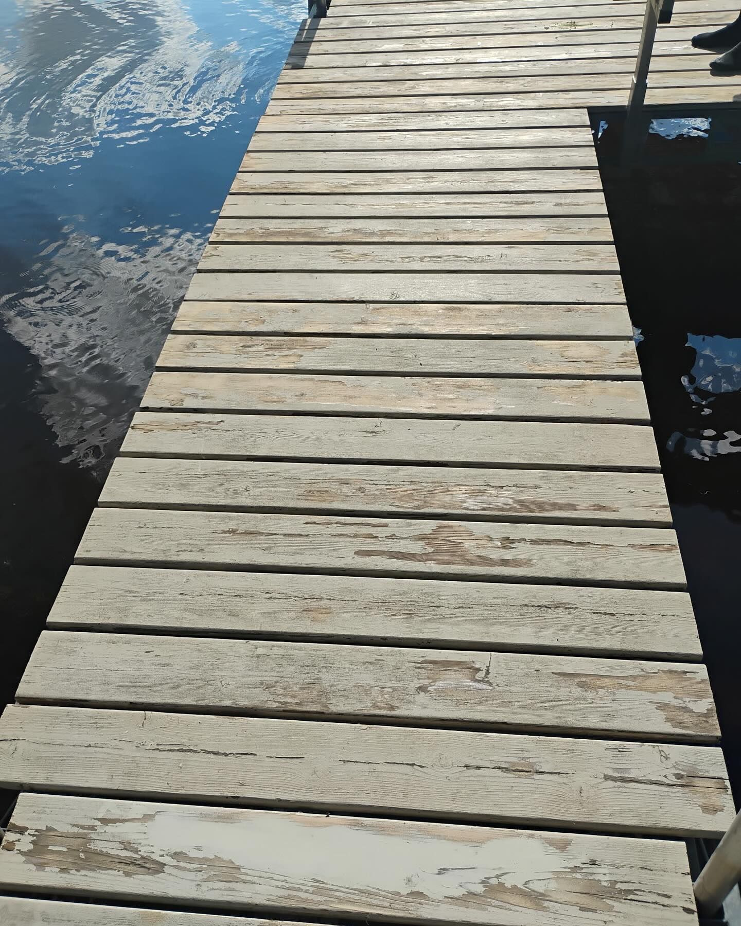 Wooden dock extends over dark water. The dock is made of weathered, light-colored planks.