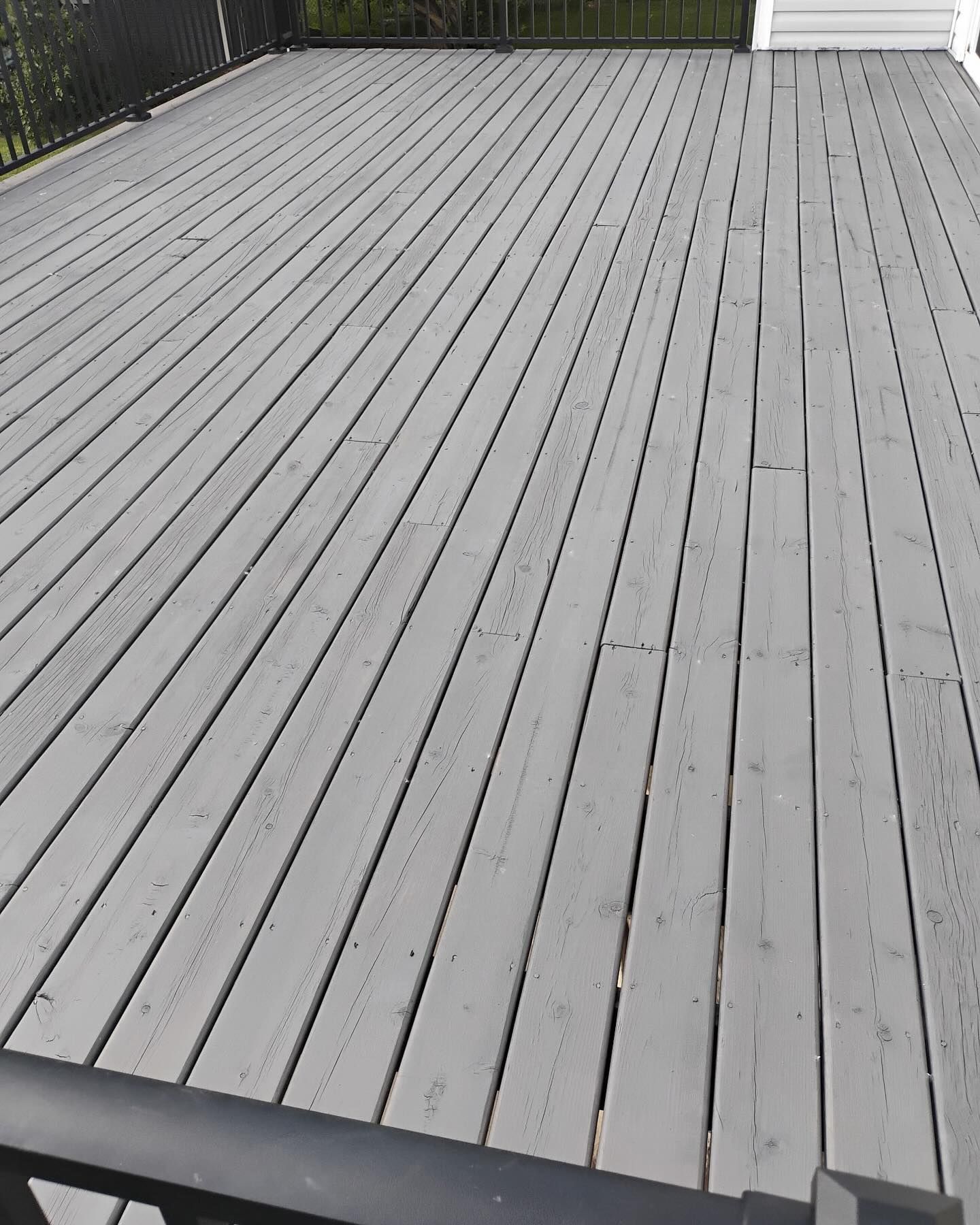 Gray wooden deck with black railing, angled perspective from above.