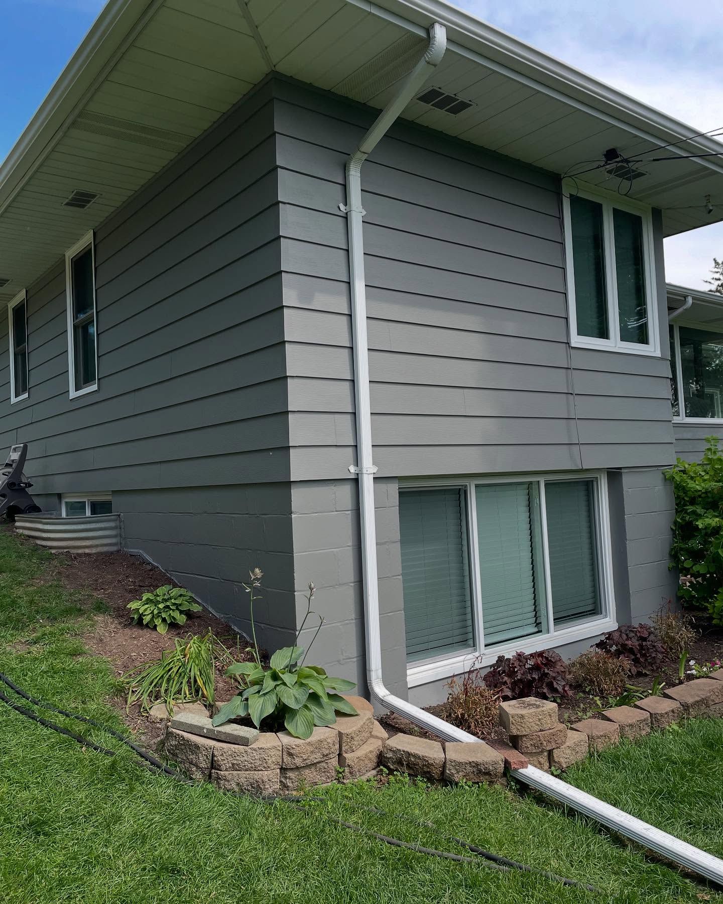 Gray house with white trim and gutters, featuring horizontal siding and a small garden bed.