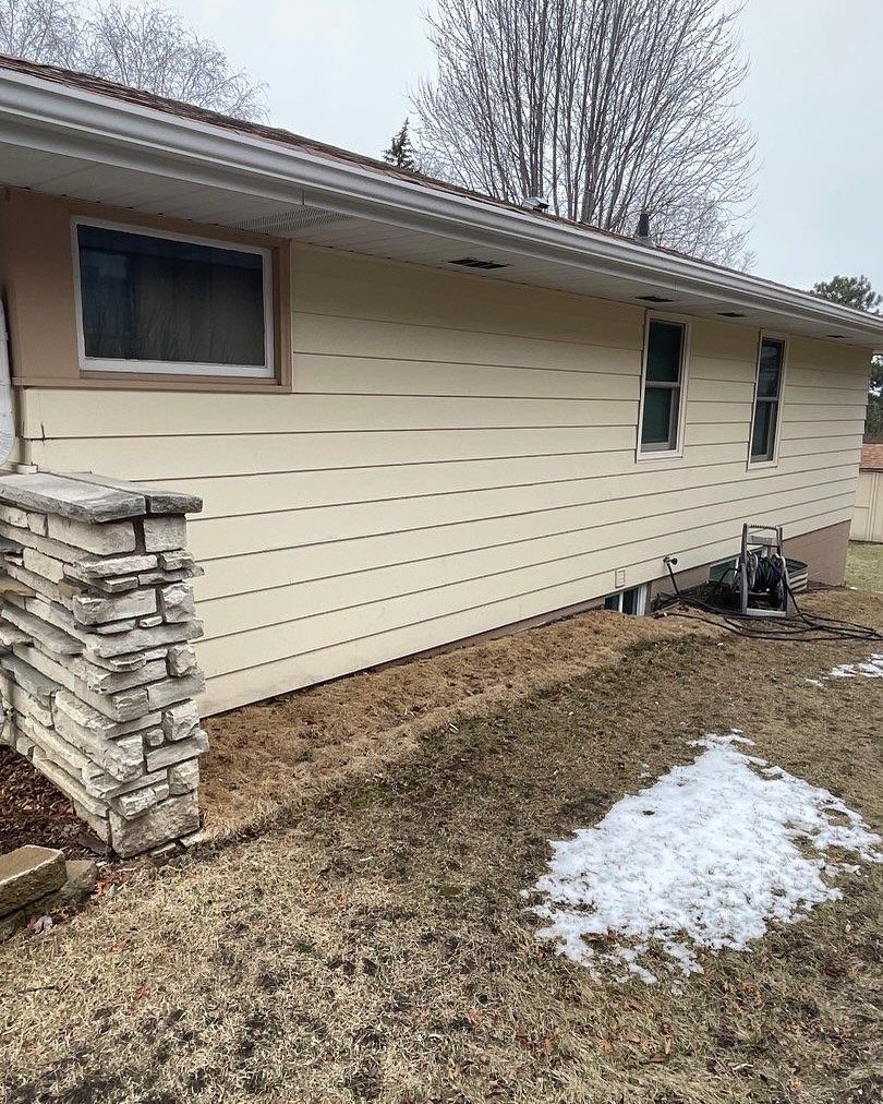 Beige house with tan trim and small windows; a low retaining wall and a patch of snow in the yard.