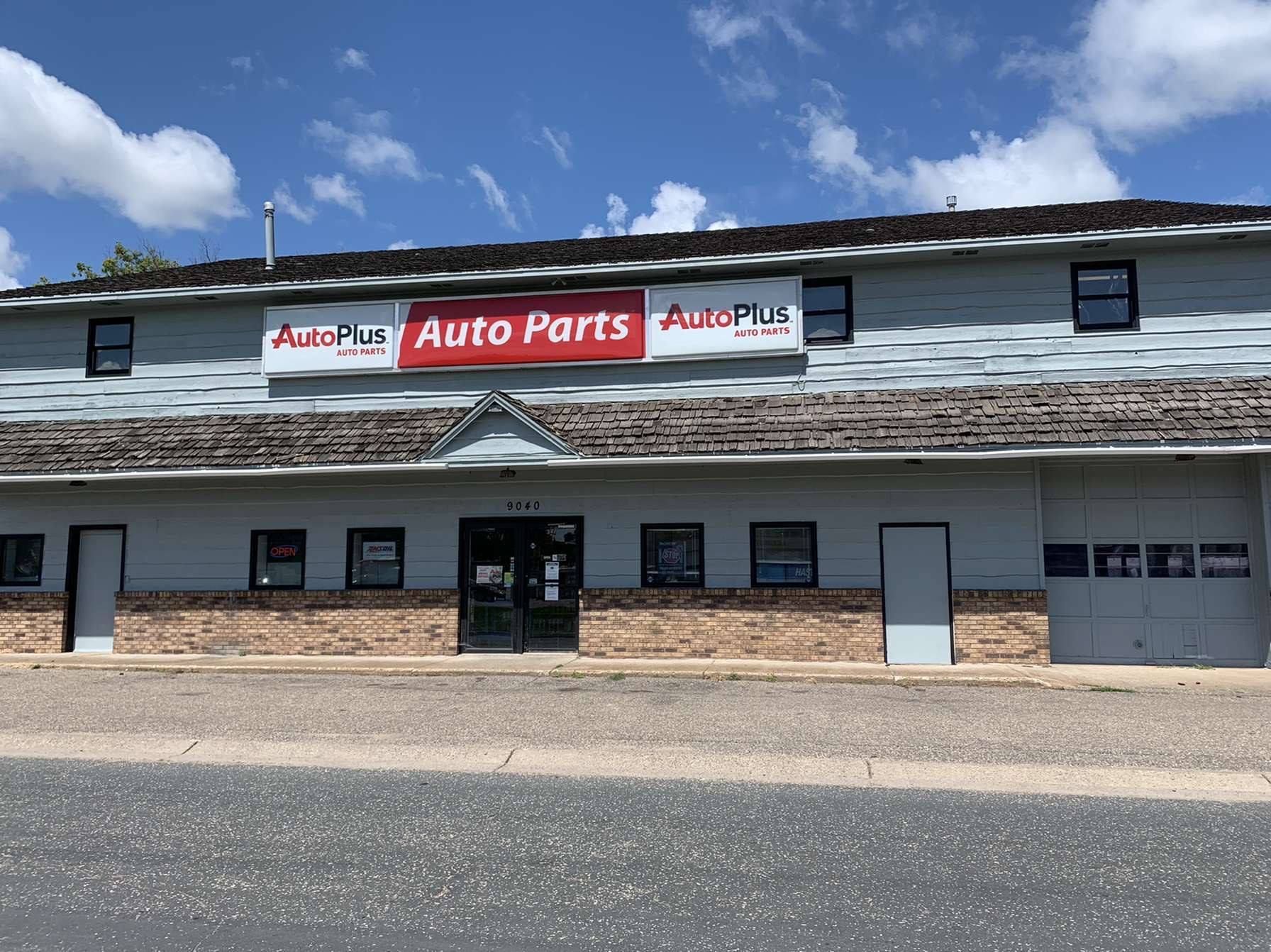 Auto Plus Auto Parts store exterior on a sunny day. Gray building with a brick facade and signage with the company's logo.