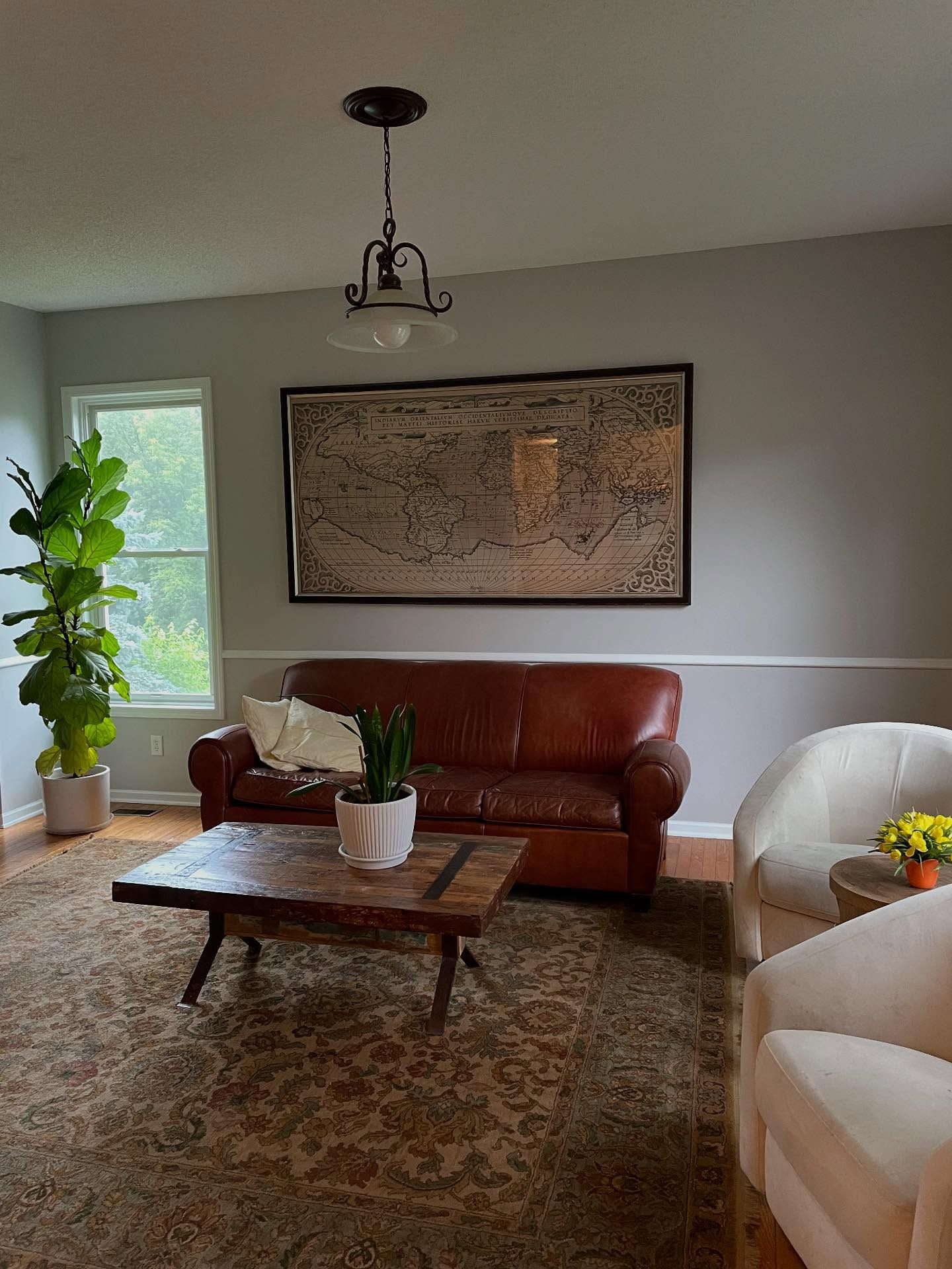 Living room with a leather couch, area rug, and large abstract art on a gray wall. A Fiddle Leaf Fig stands near a window.