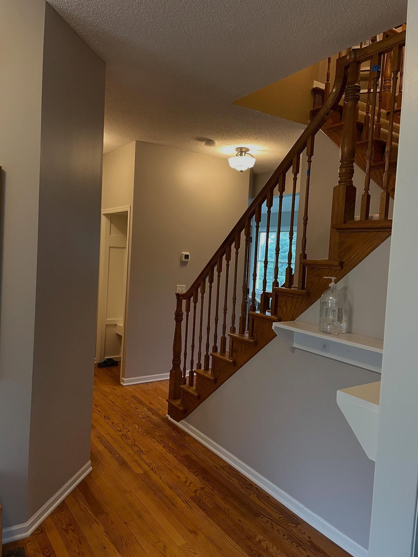Hallway with wooden floors and staircase. The walls are a muted gray, the staircase is wood. A white door is at the hallway's end.