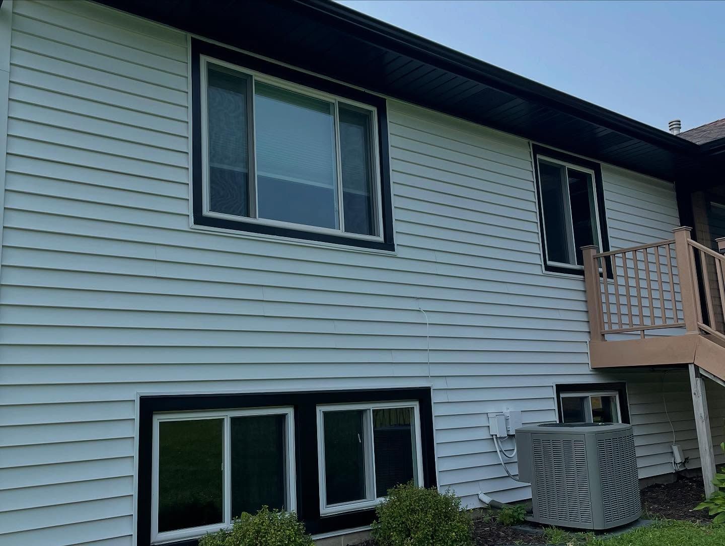 White siding of a house with black window frames and trim. An air conditioning unit sits below a window.