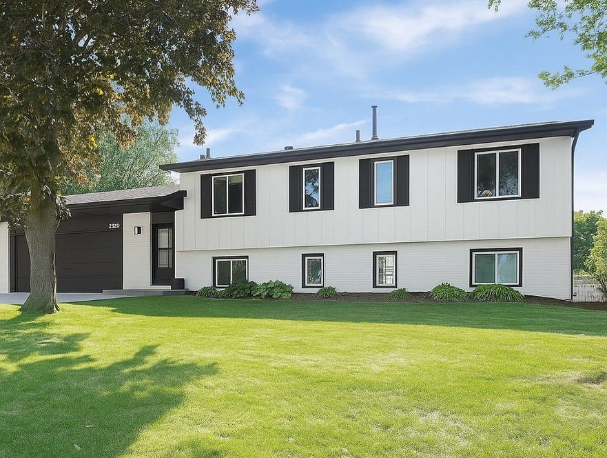 Two-story white house with black trim and shutters, set on a green lawn under a blue sky.