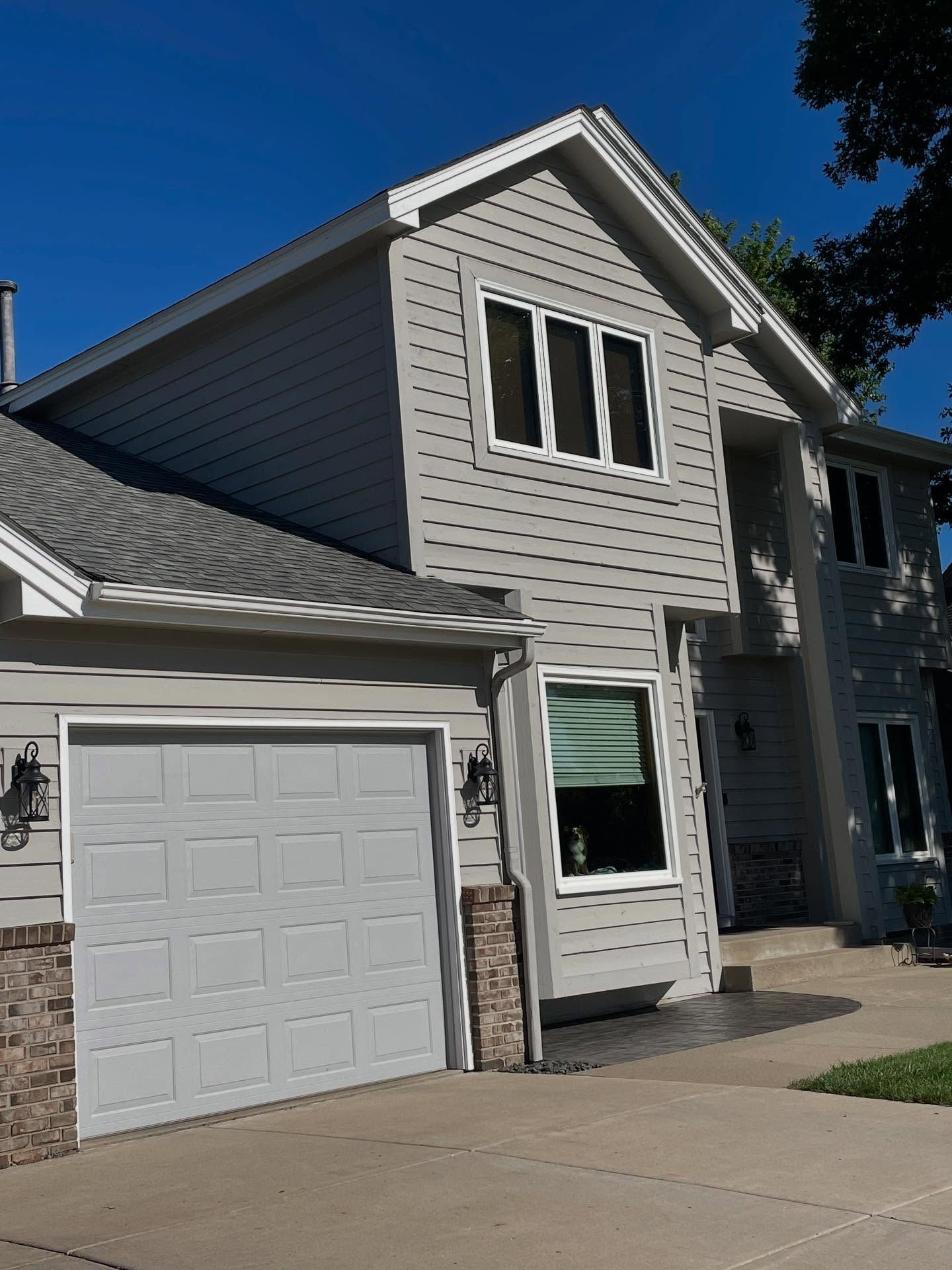 Gray two-story house with white trim, garage, and blue sky.  The house has a stone accent and a gray garage door.
