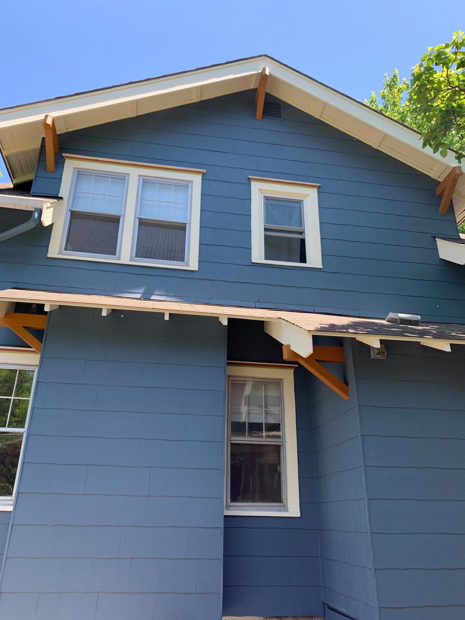 Blue house exterior with windows, wooden supports, and sections of missing roof trim, under a bright blue sky.