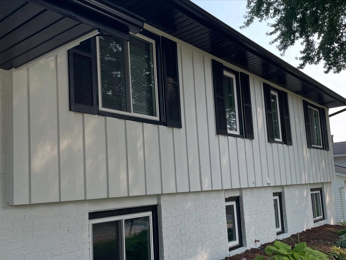 Exterior view of a two-story house with white siding, black shutters, and a dark roof. Windows are outlined in black.