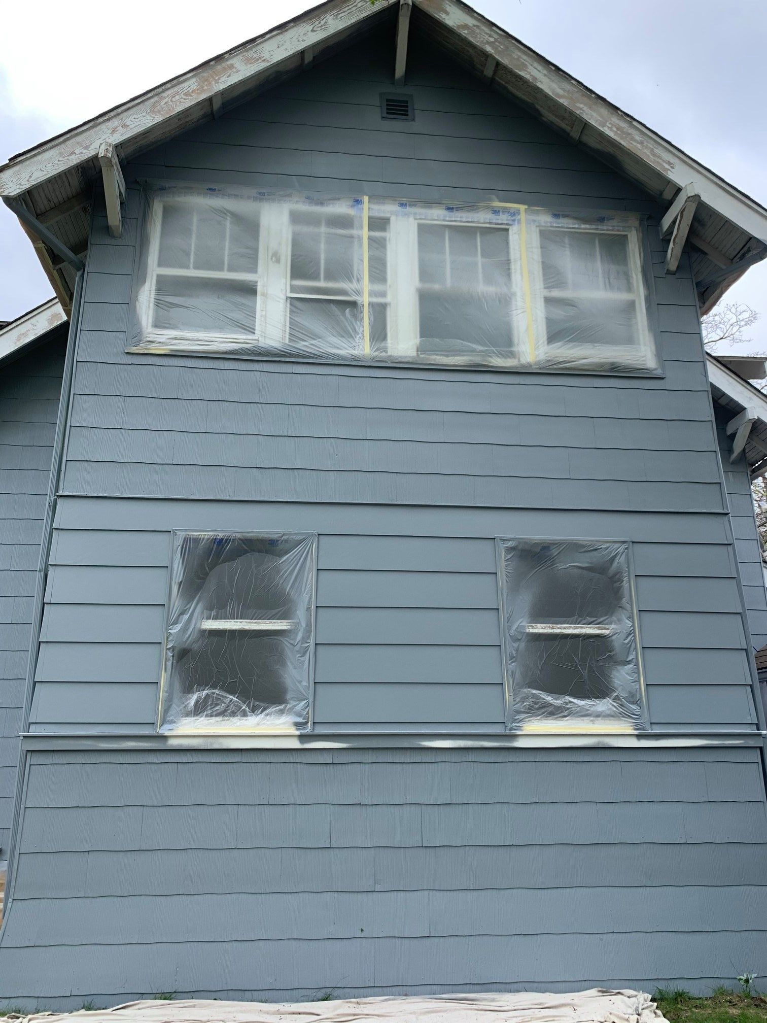 Blue house with taped windows, ready for painting, against an overcast sky.