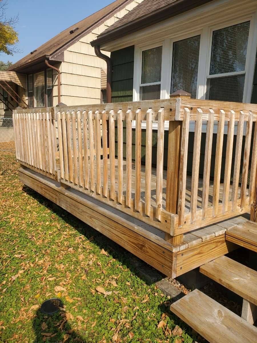 Wooden deck with a railing next to a house, with steps leading down to a grassy yard.