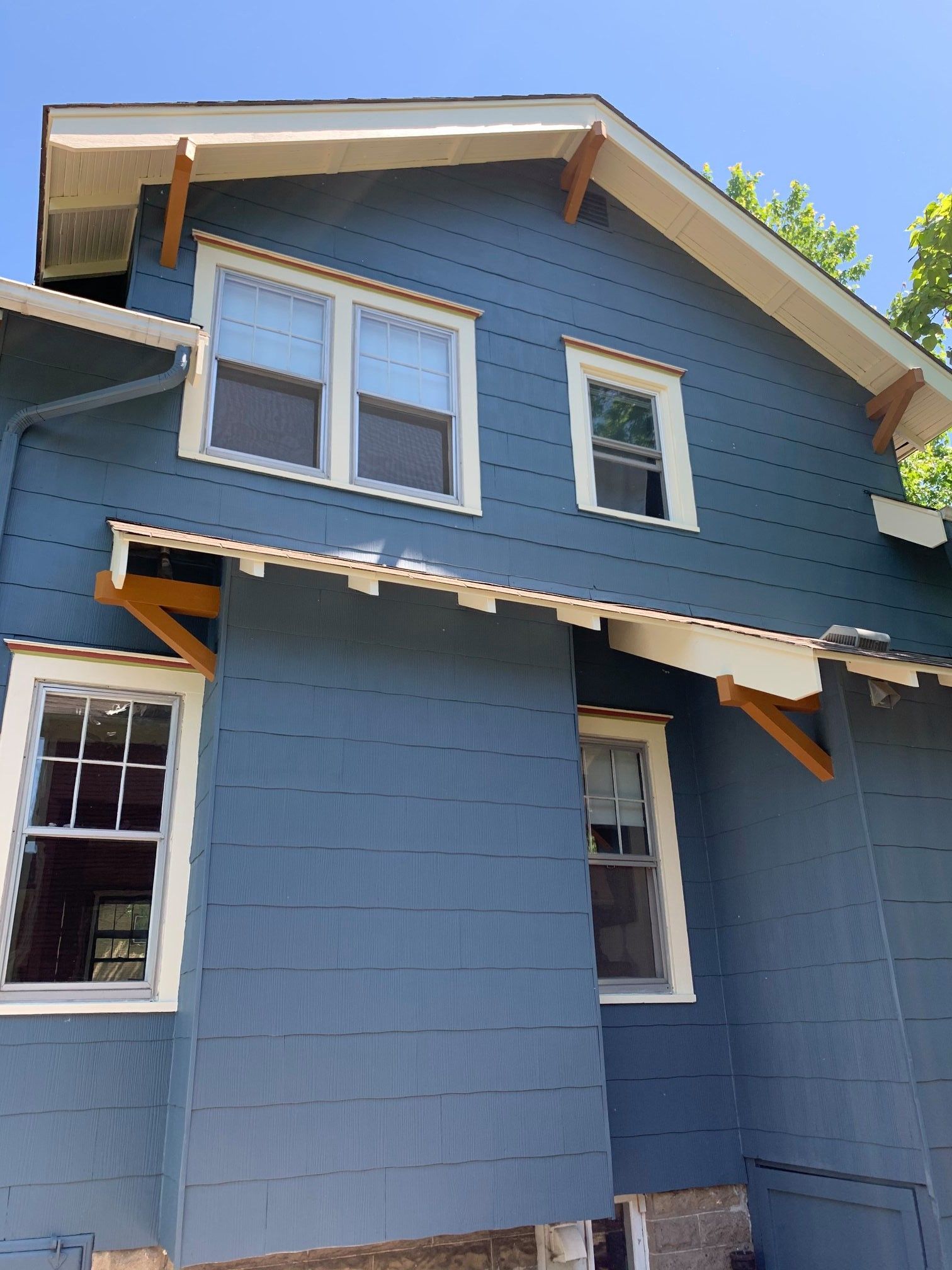 Blue house exterior with white trim, windows, and wooden supports under the roof. Sunny day.