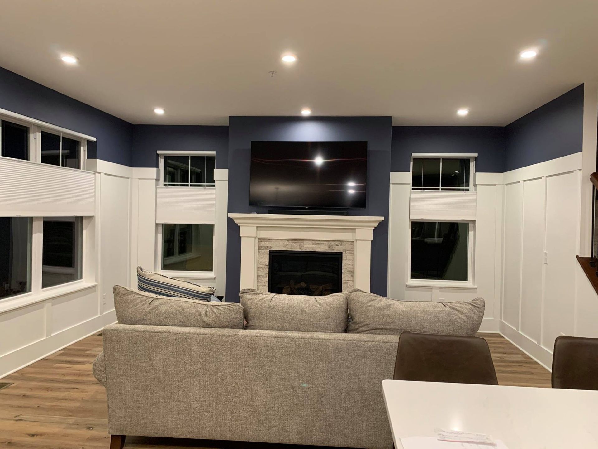 A modern living room with a gray couch, fireplace, and a large TV centered on a navy blue accent wall with white paneling.