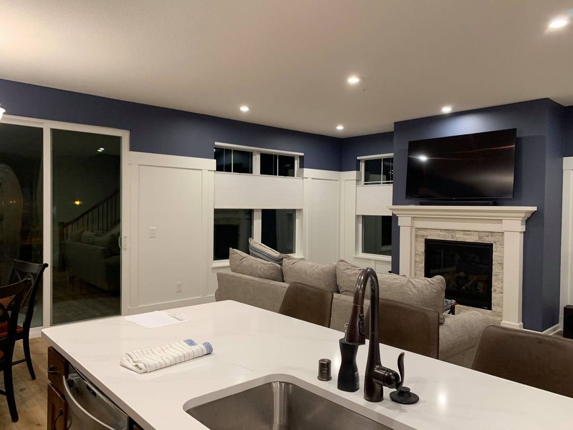 Modern kitchen with a large island, dark blue walls, and a fireplace with a mounted TV. A sliding glass door leads to outside.