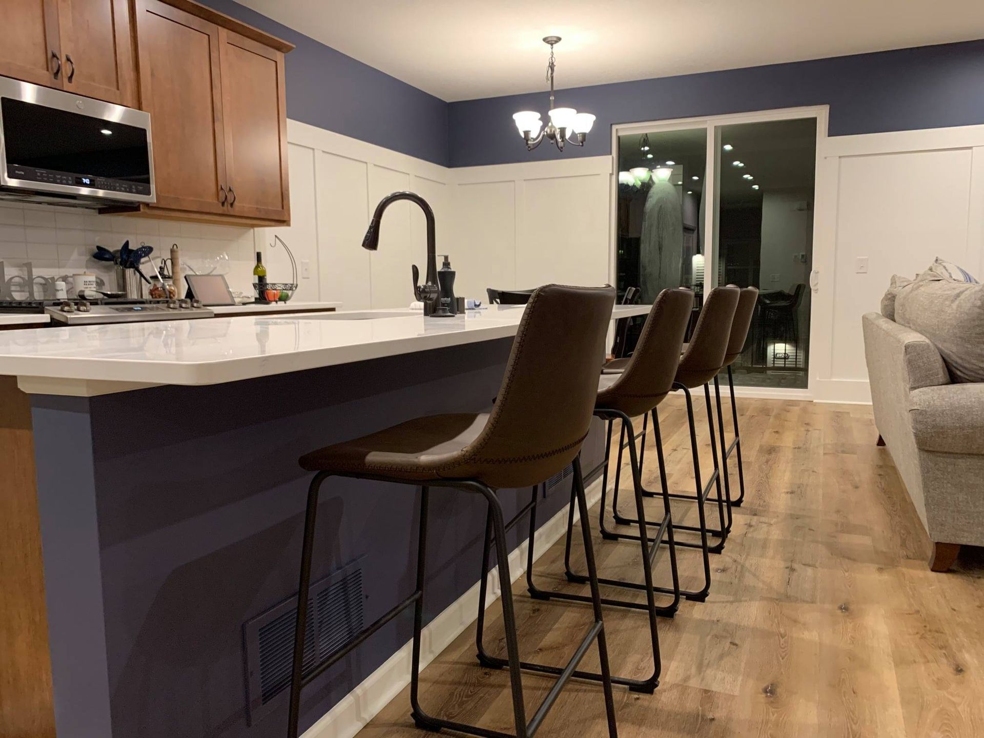 A kitchen with a countertop bar and brown stools. Dark blue walls, wood cabinets, and a sliding glass door are visible.