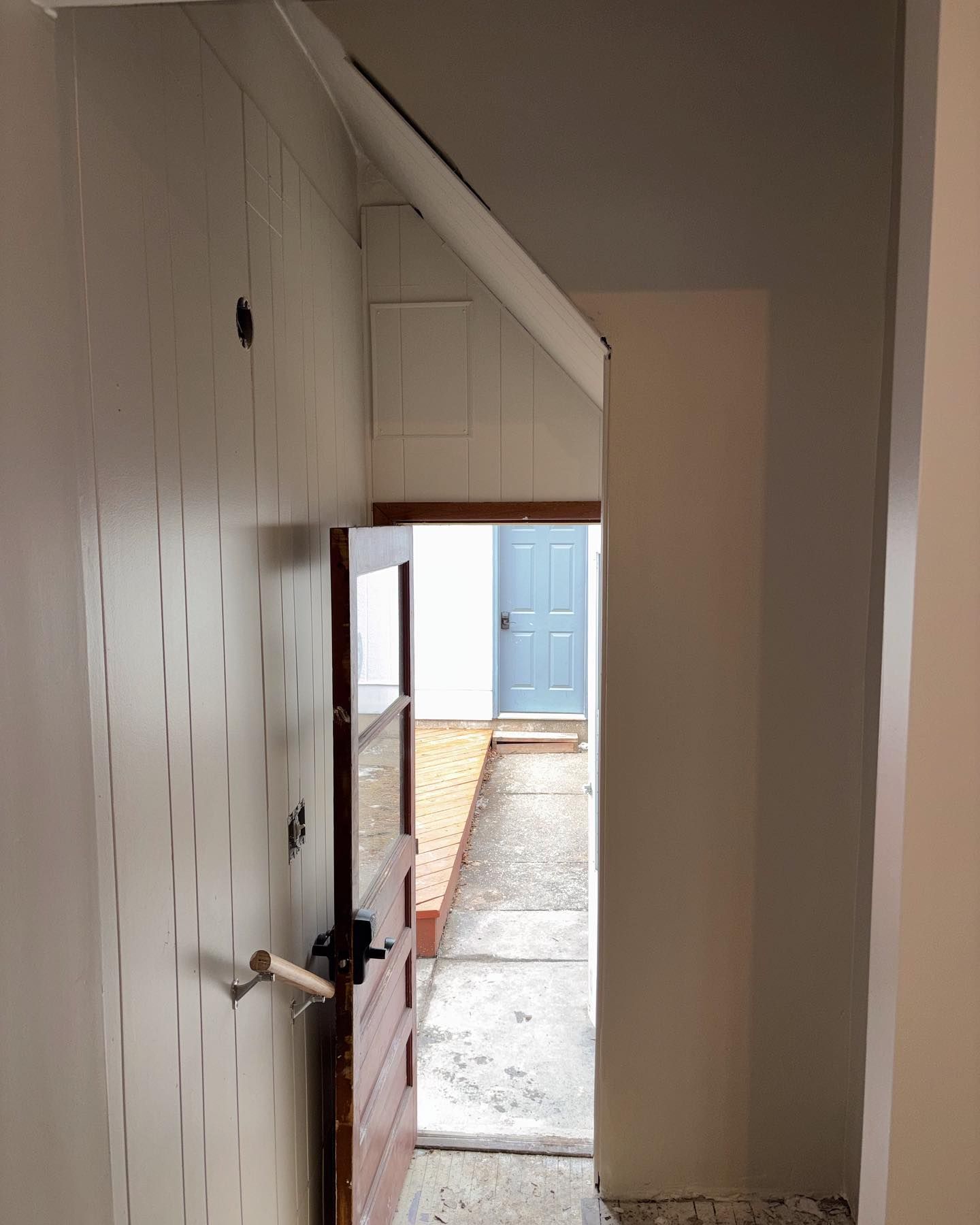 An interior view through an open wooden door, leading to a hallway with a blue door at the end.