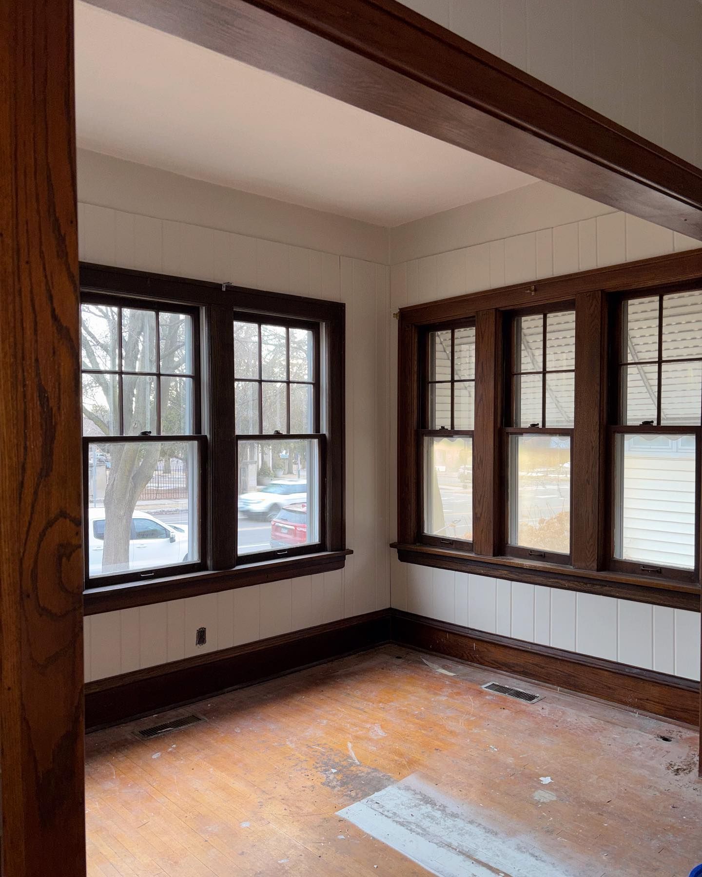 Empty room with wood trim windows and hardwood floors. White wainscoting on walls, and dark wood beams and window frames.