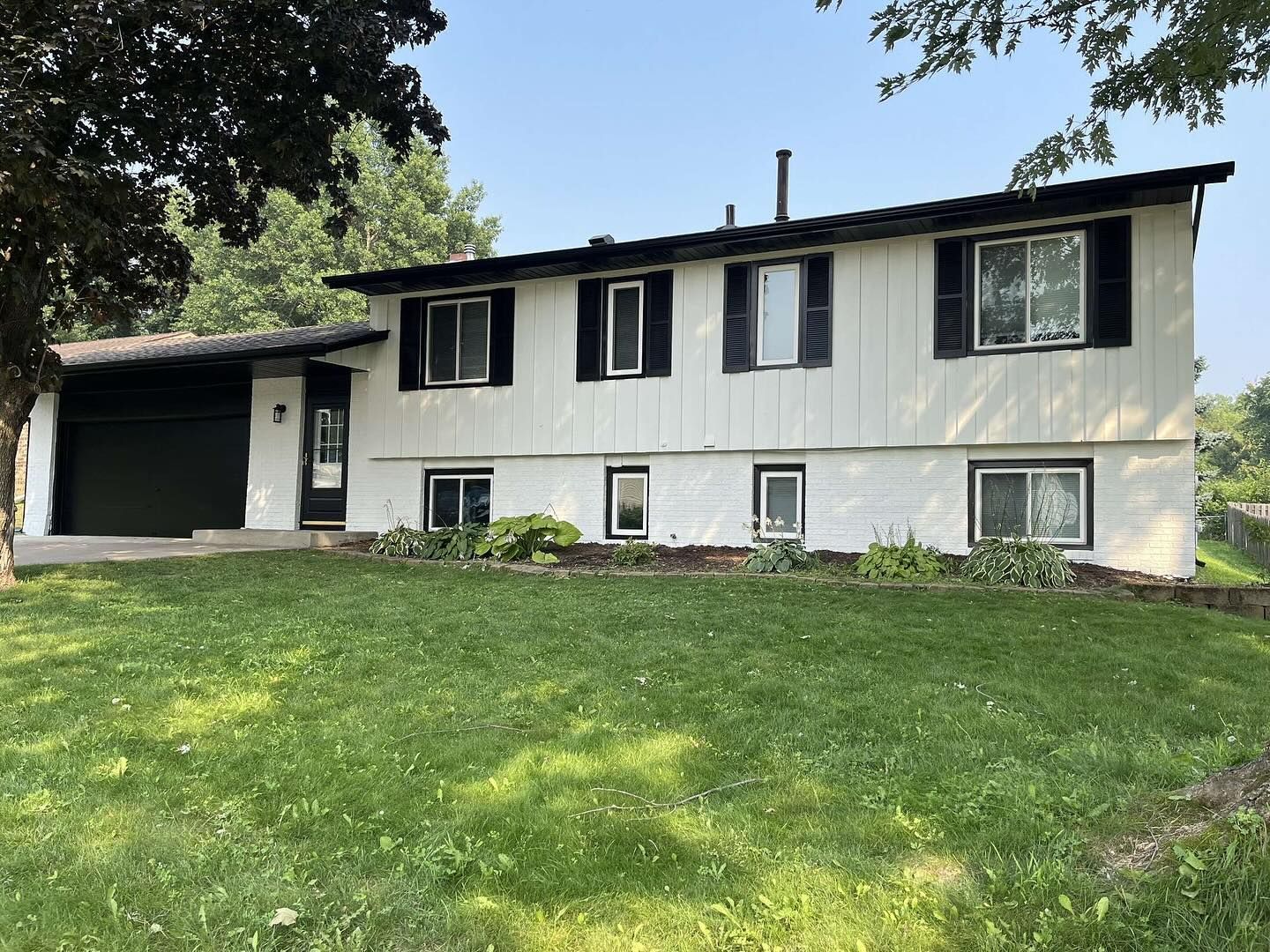 White two-story house with black trim and garage. Green lawn in front.