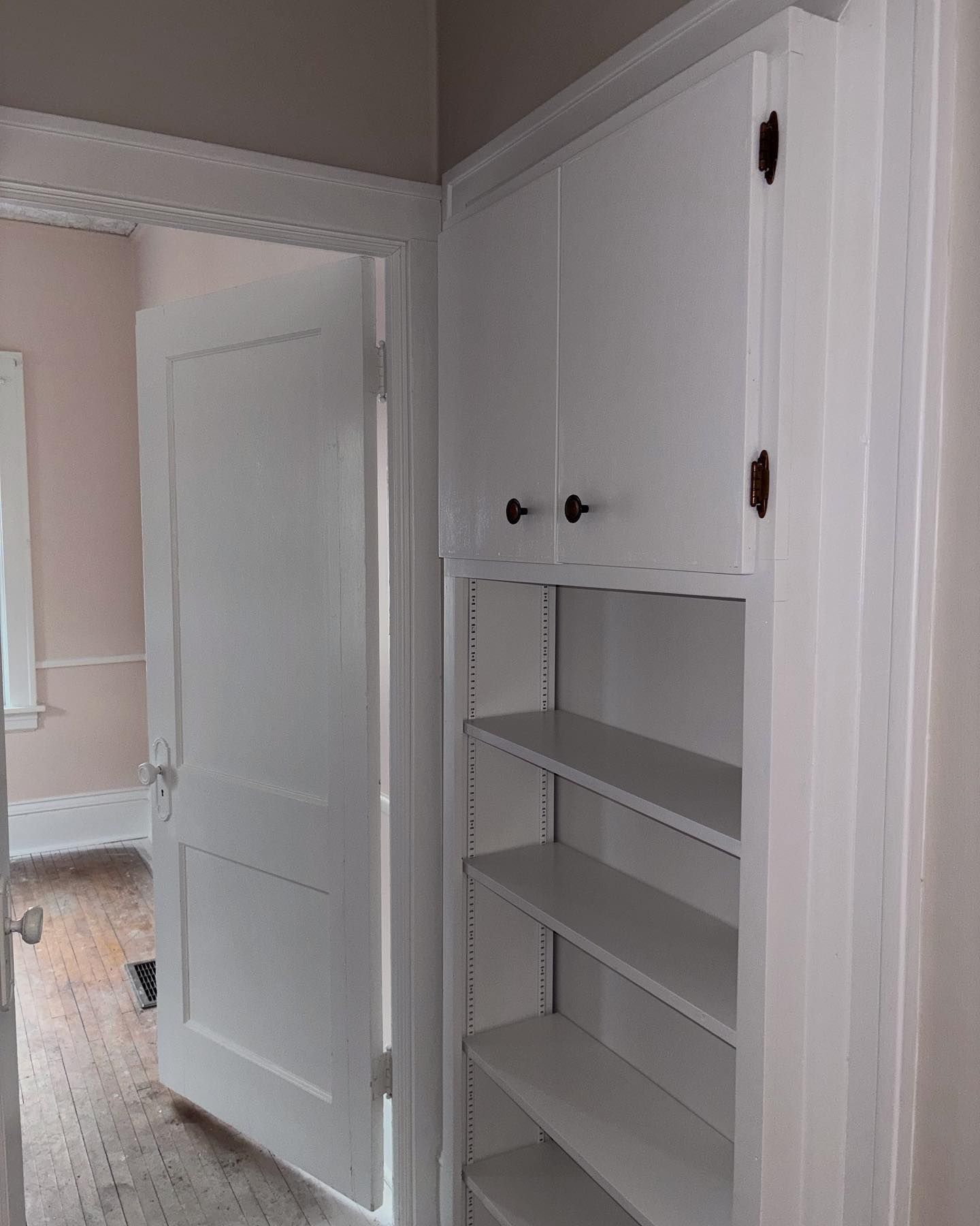 White built-in storage with open shelves and upper cabinets, next to an open white door leading to a room.