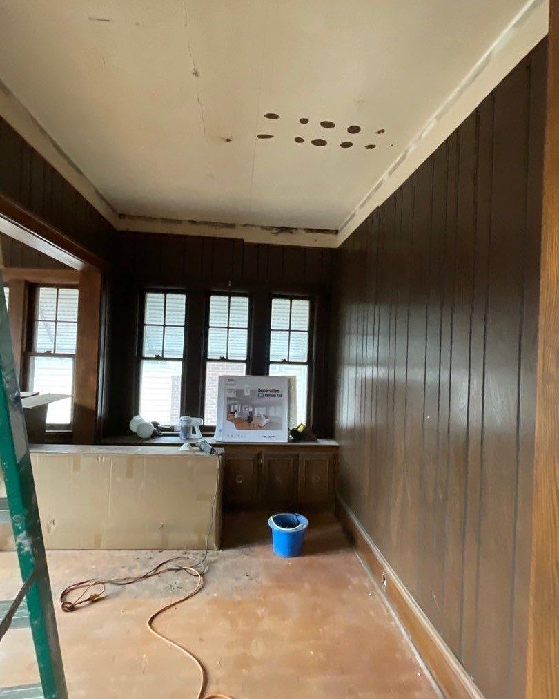 Interior room with dark wood paneling and ceiling damage.  A ladder, cardboard box, and tools are present, suggesting renovation.