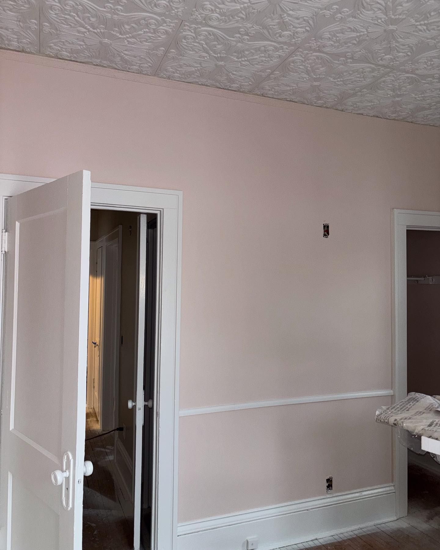 A room with pink walls, white trim, and a textured ceiling. Two doorways lead to other rooms.