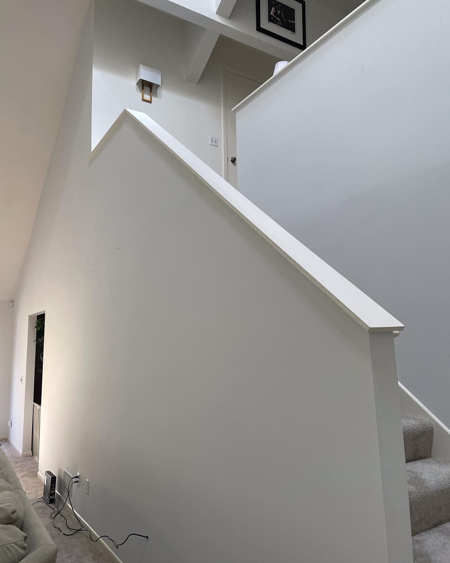 A white stairwell with a minimalist design. The stairs have a carpet runner and a wall on the side with a handrail.