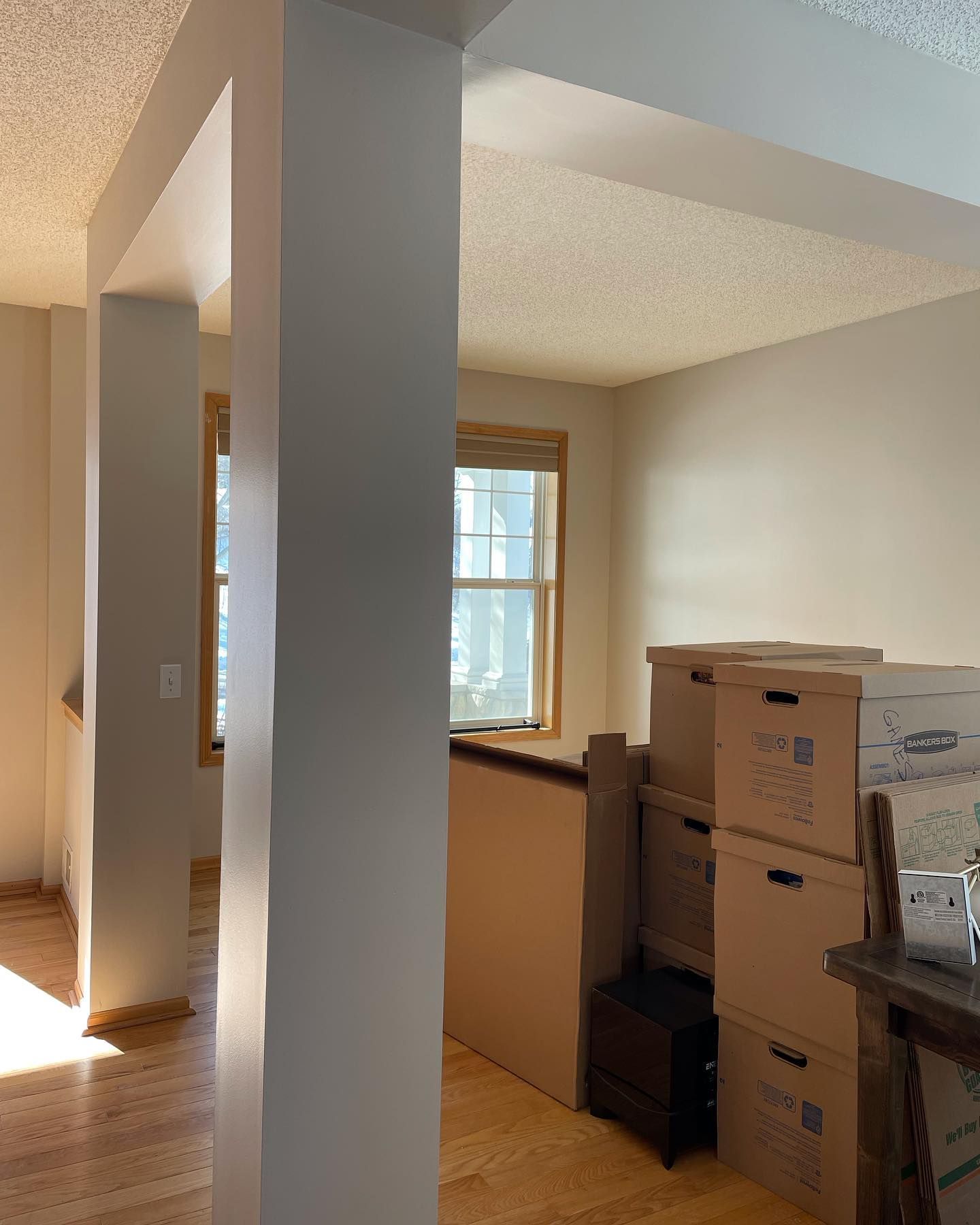 A light-filled interior shows a doorway framed by two pillars. Boxes and a staircase sit on the right, with windows visible in the background.