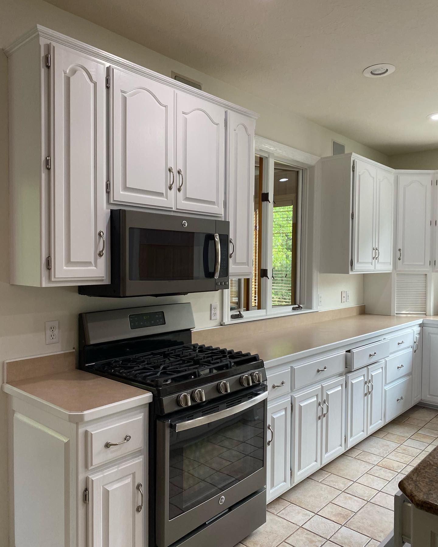 White kitchen cabinets, with a built-in microwave above a gas range. Counters run along a window.