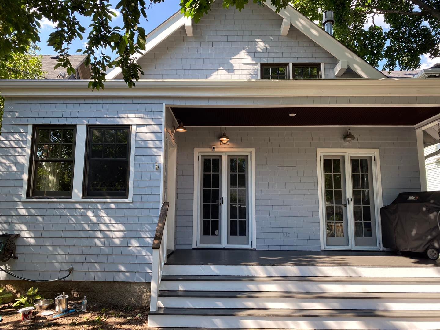 Blue-gray shingled house with white trim.  French doors lead to a porch with outdoor lights.
