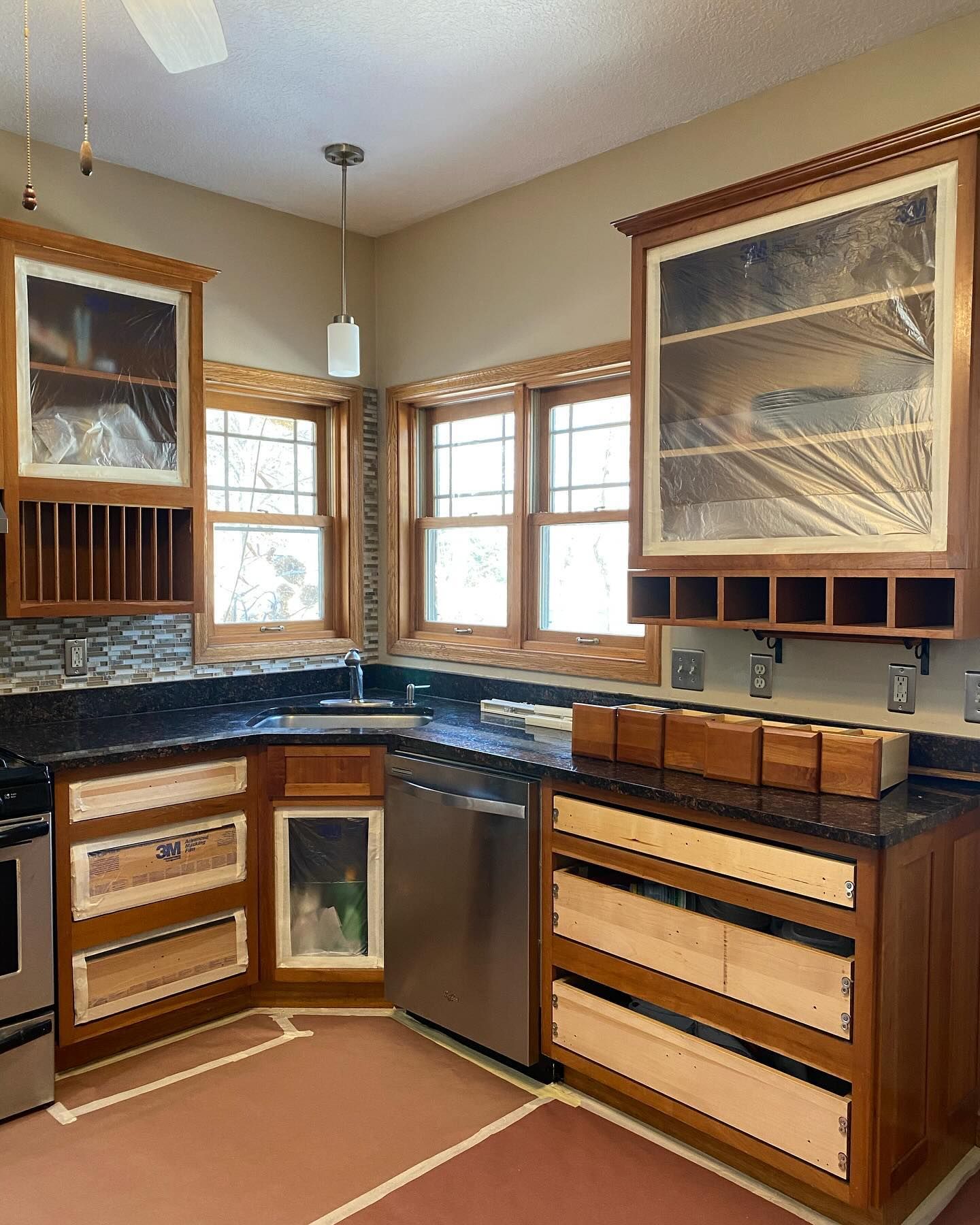 Kitchen remodel in progress; cherry cabinets, black countertops, stainless steel appliances, and protective plastic covering some areas.