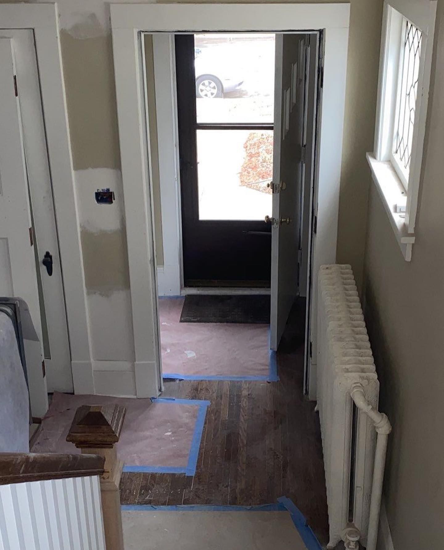 Hallway with dark wood floors, open black door to the outside, white trim, and radiator.