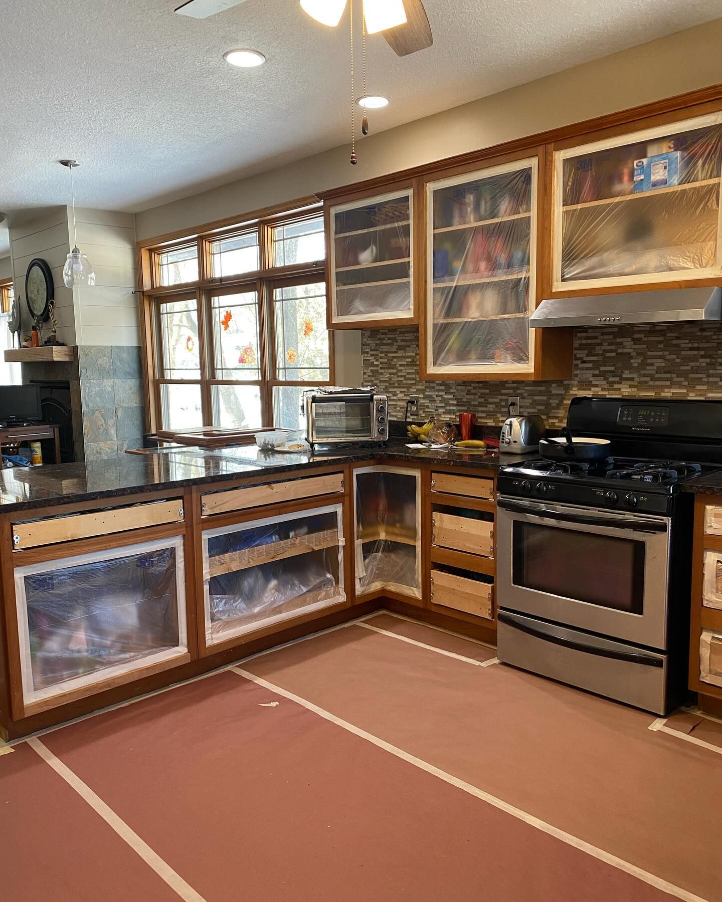Kitchen undergoing renovations: cabinets covered in plastic, new countertops, and the floor covered in protective sheeting.