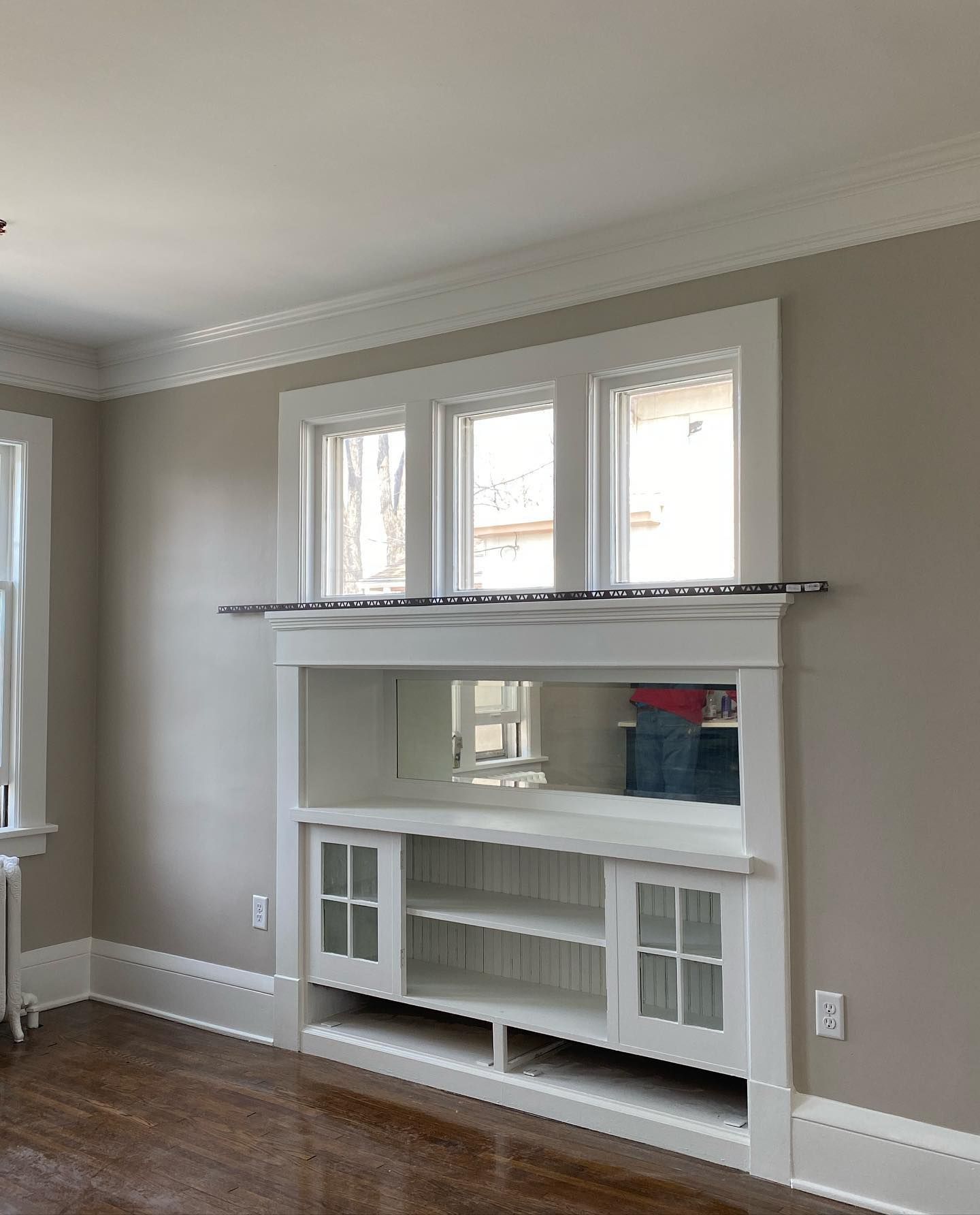 Built-in white bookshelf with three windows above it. The bookshelf has a mirrored back and two cabinets. The walls are gray.