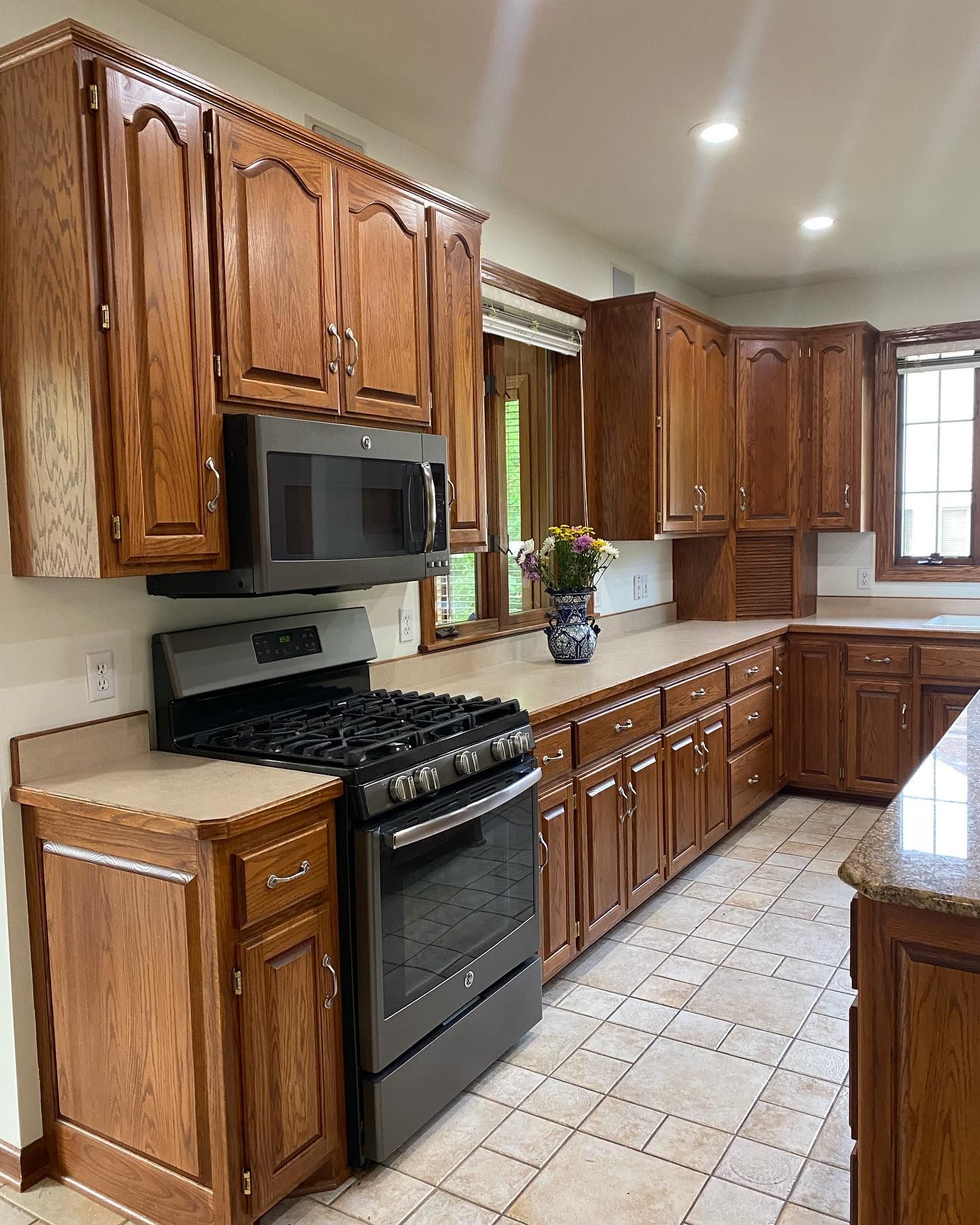 Brown kitchen cabinets with a dark stove and microwave, beige countertops, and a tiled floor.