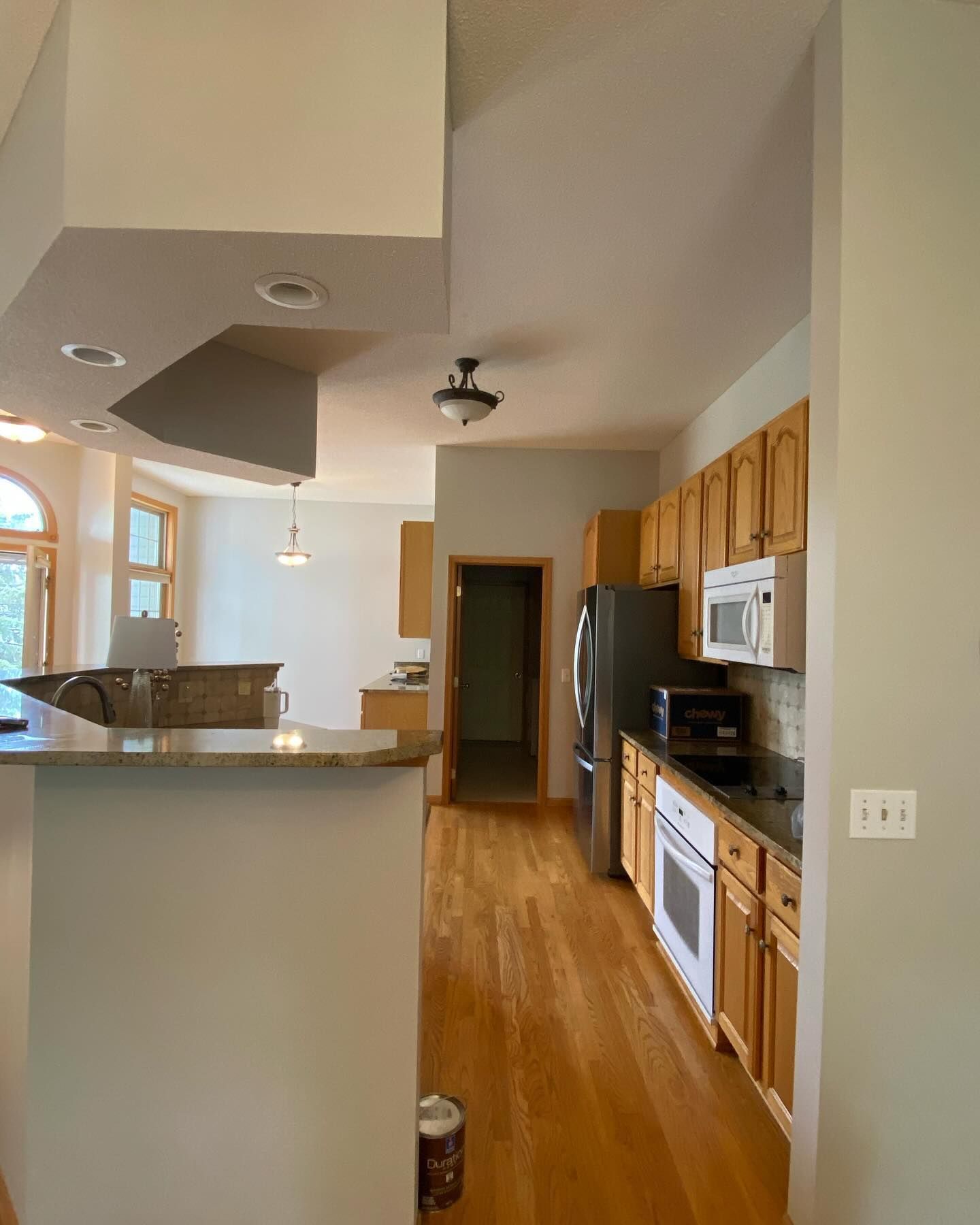 A kitchen with light wood cabinets, stainless steel appliances, and hardwood floors. A half-wall with a countertop separates the kitchen from a dining area.