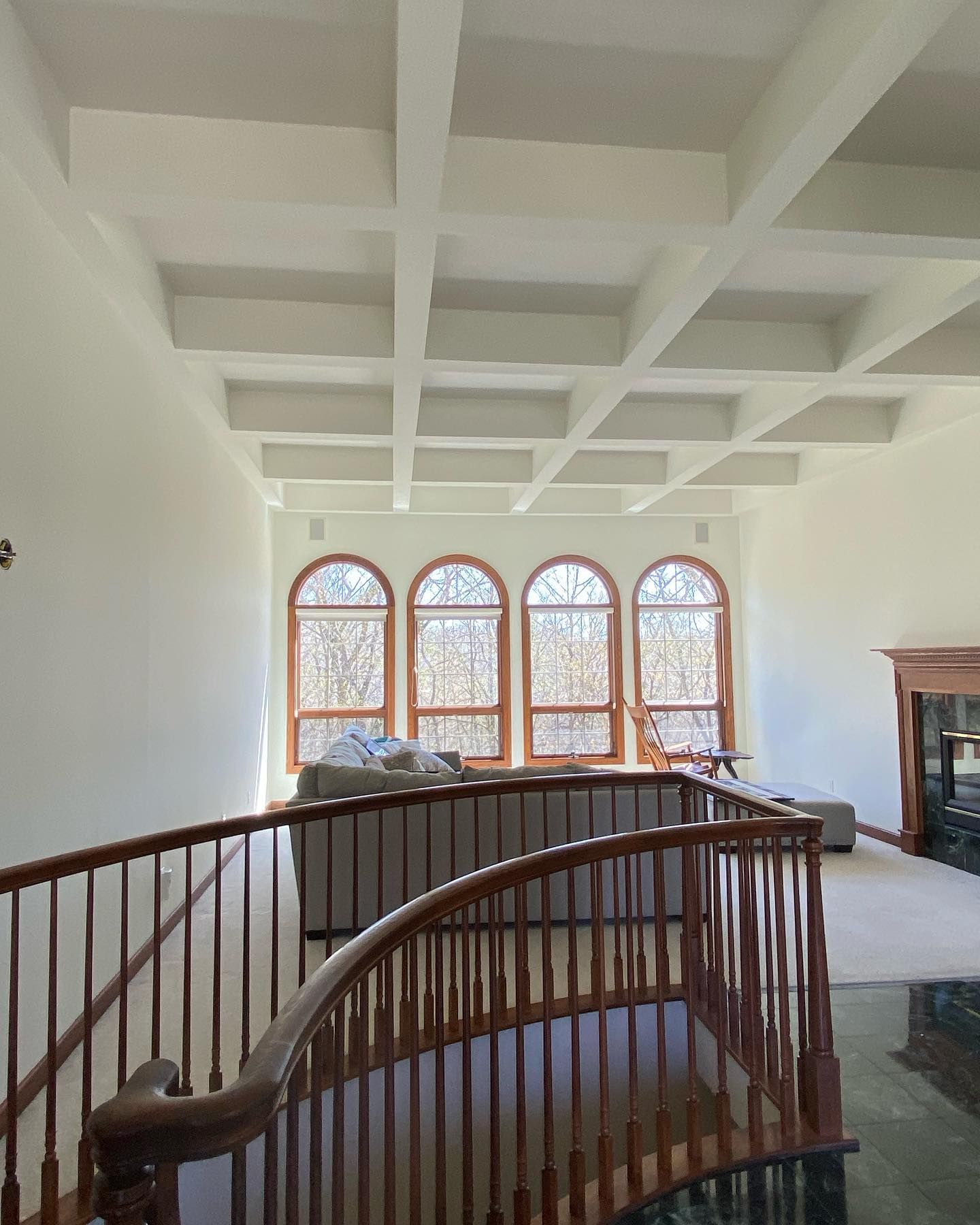 Interior view of a room with high ceilings, a curved staircase, arched windows, and a coffered ceiling.