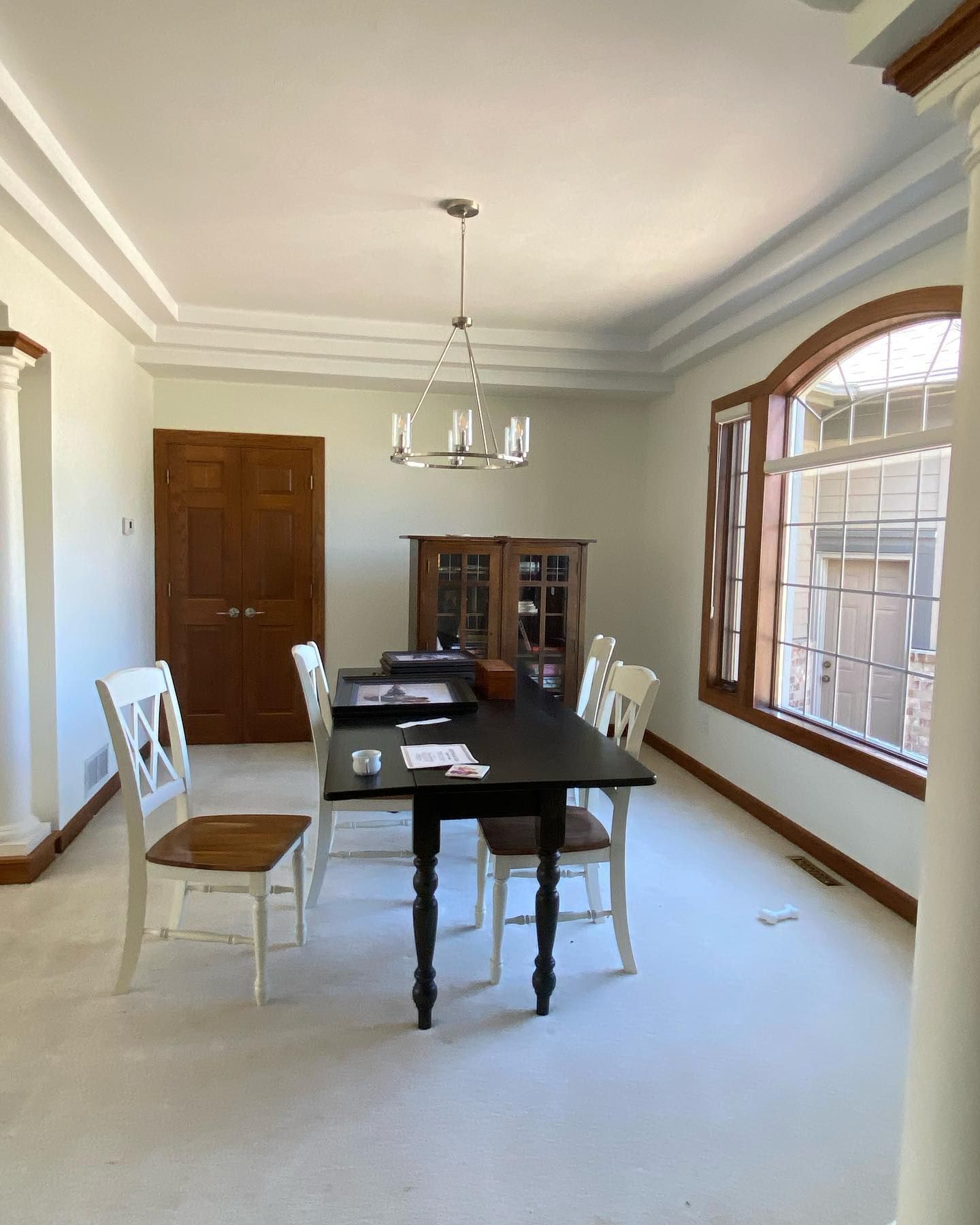 Dining room with a dark table, white chairs, a wooden cabinet, and a chandelier. There's a large arched window on the right.