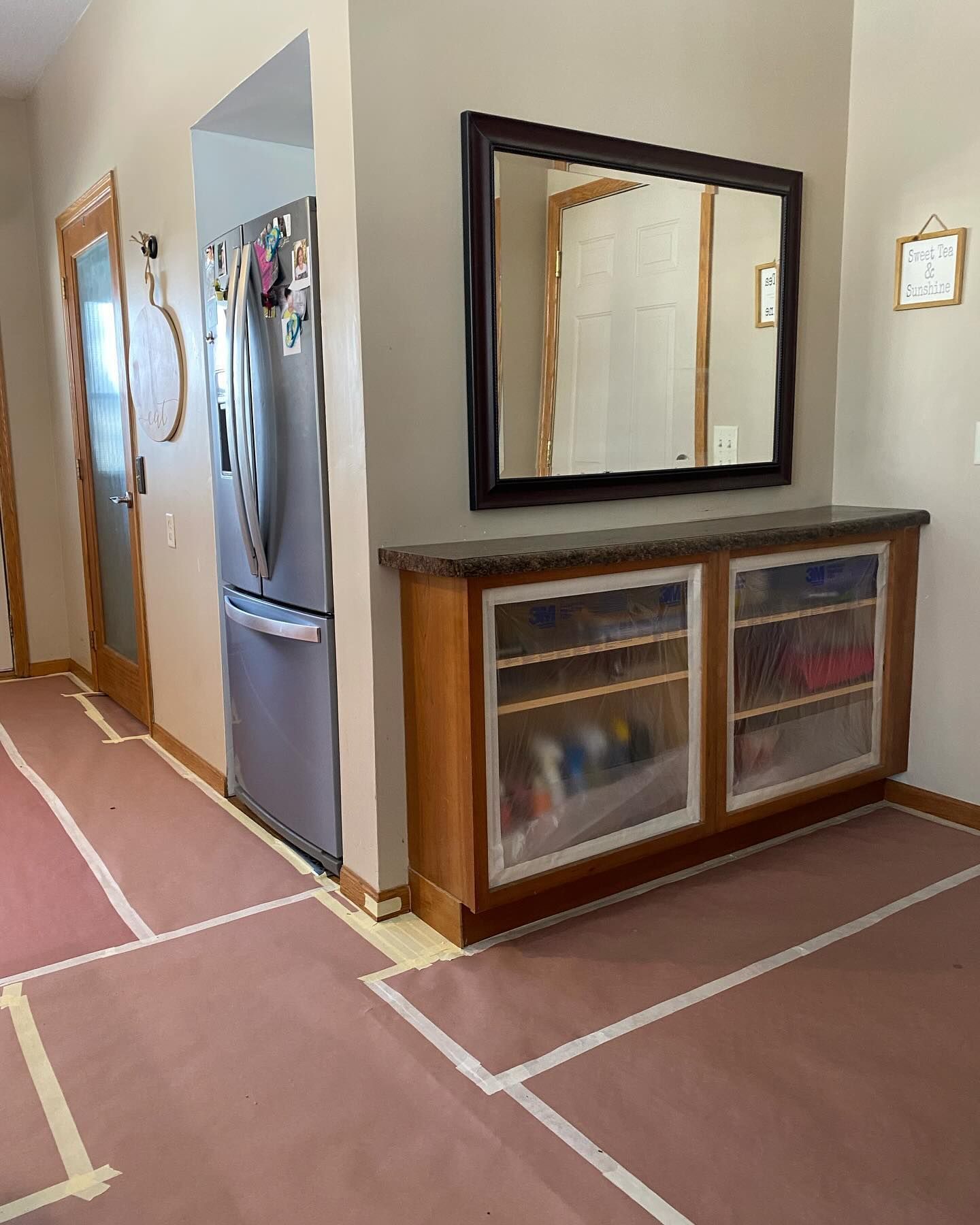 A hallway with a refrigerator, built-in cabinet with a mirror above it, and protective floor covering.