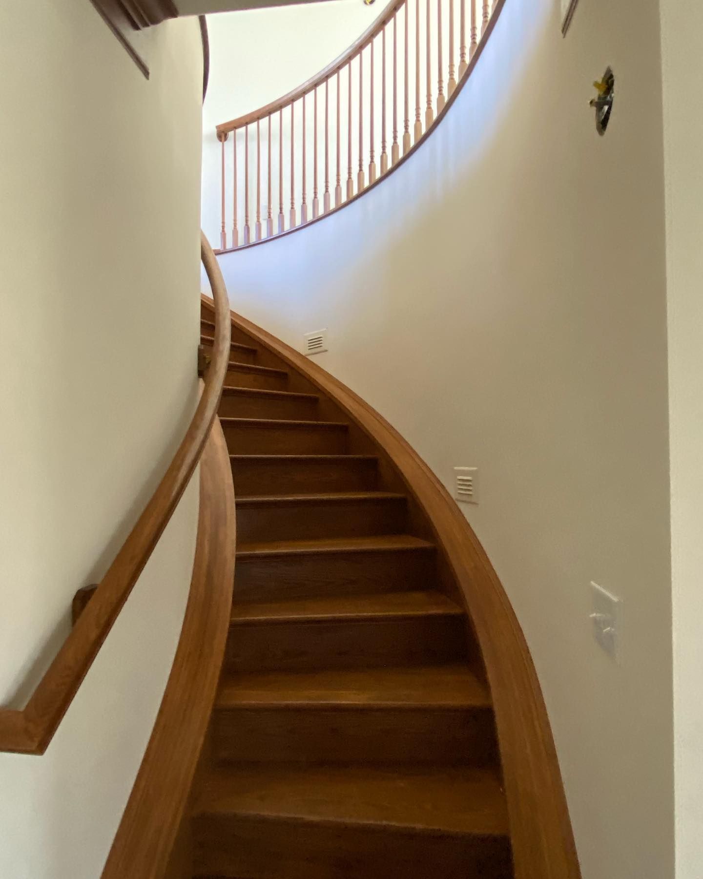 Wooden curved staircase ascending, with a wooden railing, and white walls.