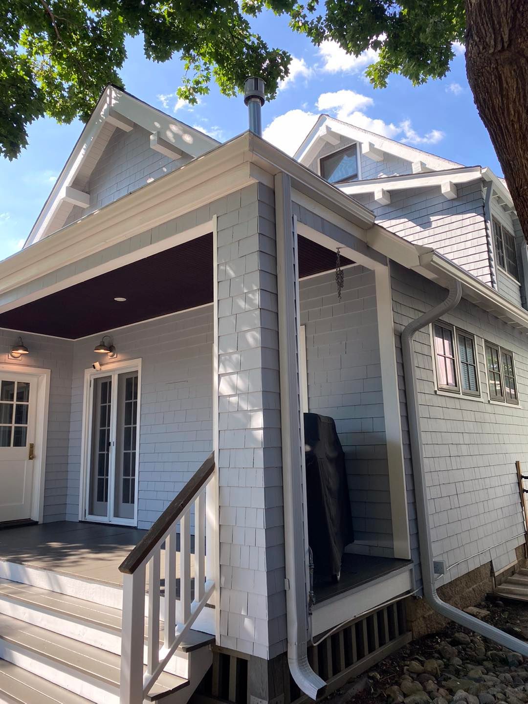 Light blue house with a porch, white trim, and a silver chimney. Wooden steps lead to the front door under a deep red porch ceiling.
